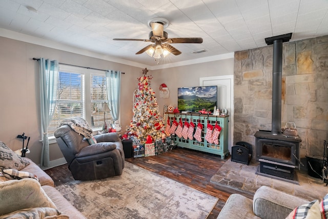 living room with ceiling fan, crown molding, a wood stove, and dark wood-type flooring