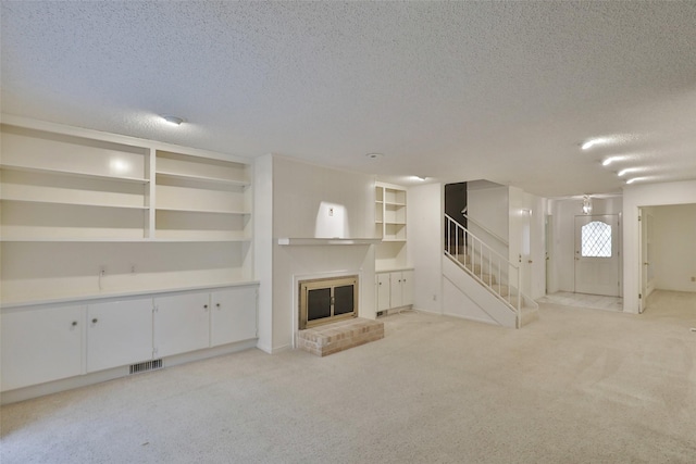 unfurnished living room featuring light carpet, a fireplace, built in features, and a textured ceiling