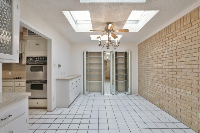 kitchen with white cabinets, ceiling fan with notable chandelier, stainless steel double oven, and brick wall