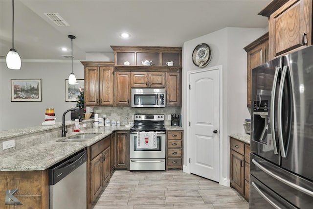 kitchen with sink, light stone counters, kitchen peninsula, decorative light fixtures, and appliances with stainless steel finishes