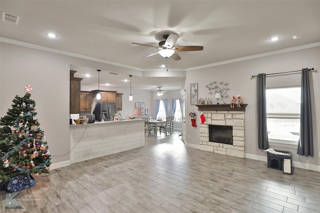 living room with ceiling fan, a stone fireplace, and ornamental molding