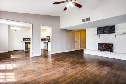 unfurnished living room featuring ceiling fan with notable chandelier, dark hardwood / wood-style flooring, a fireplace, and a high ceiling