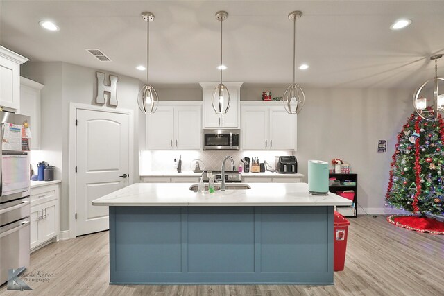 kitchen featuring decorative light fixtures, white cabinetry, sink, stainless steel appliances, and a center island with sink