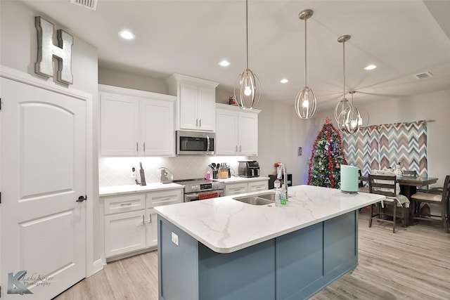 kitchen featuring sink, white cabinetry, decorative light fixtures, a center island with sink, and appliances with stainless steel finishes