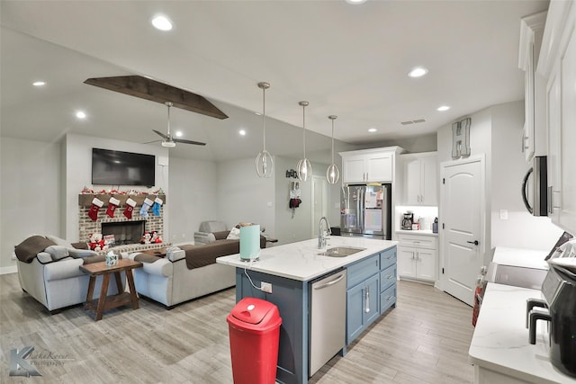 kitchen featuring sink, decorative light fixtures, stainless steel appliances, a kitchen island with sink, and white cabinets