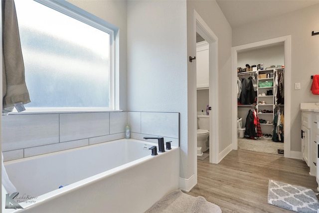 bathroom with a healthy amount of sunlight, hardwood / wood-style floors, a tub, and toilet