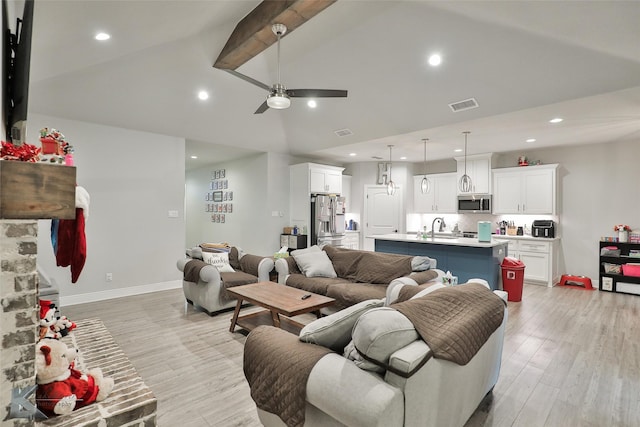 living room with ceiling fan, sink, light hardwood / wood-style floors, and vaulted ceiling with beams