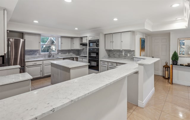 kitchen with sink, light stone counters, black appliances, a kitchen island, and kitchen peninsula