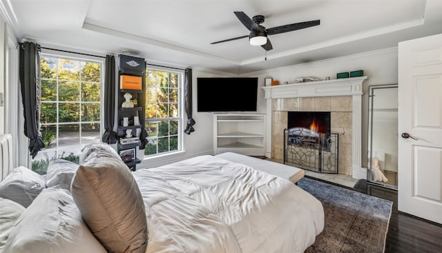 bedroom featuring dark hardwood / wood-style flooring, a tray ceiling, a tile fireplace, and ceiling fan