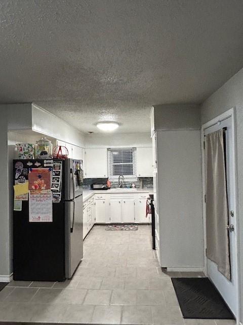 kitchen featuring a textured ceiling, black fridge, white cabinetry, and sink