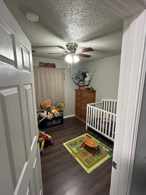 bedroom featuring a textured ceiling, a nursery area, dark wood-type flooring, and ceiling fan