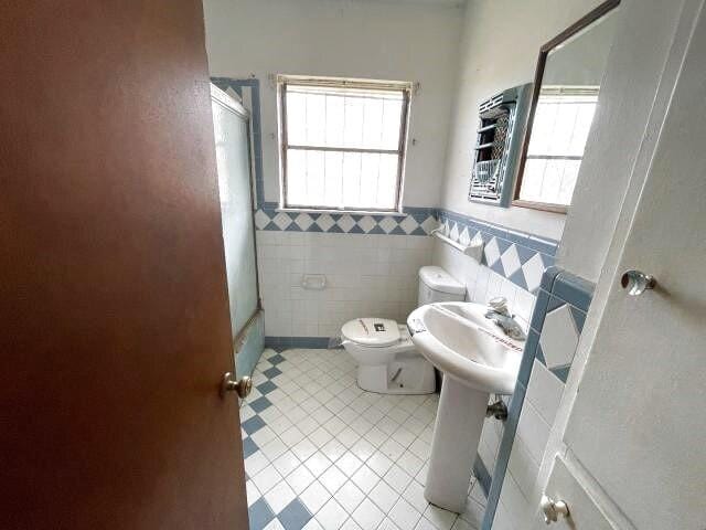 full bath with toilet, tile walls, wainscoting, and tile patterned flooring