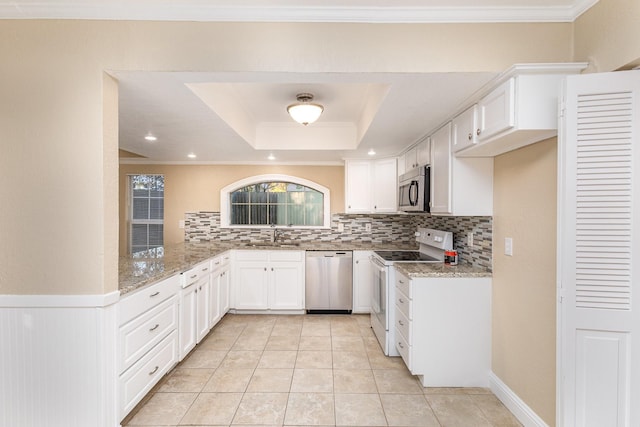 kitchen with light stone countertops, appliances with stainless steel finishes, backsplash, a tray ceiling, and white cabinetry