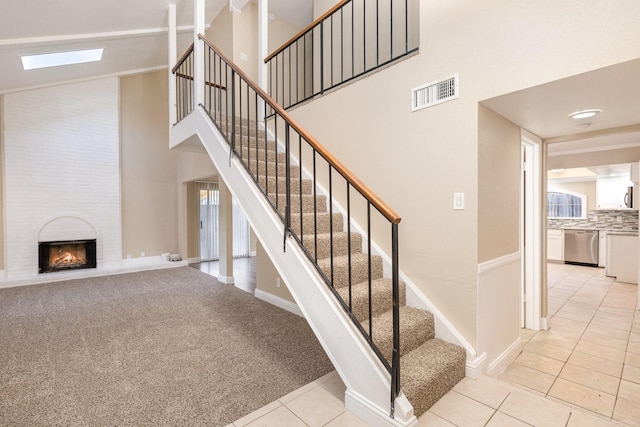 stairs featuring a skylight, a large fireplace, carpet floors, and high vaulted ceiling