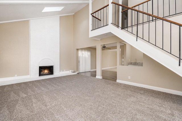 unfurnished living room featuring carpet, a skylight, a large fireplace, ceiling fan, and a high ceiling