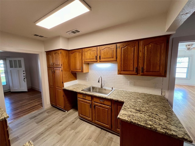 kitchen with light stone countertops, sink, ceiling fan, backsplash, and light wood-type flooring