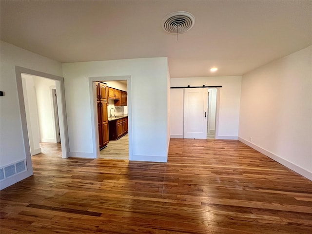 unfurnished bedroom with a barn door, light hardwood / wood-style flooring, ensuite bath, and sink