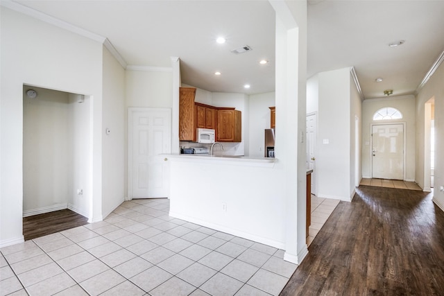 kitchen with light hardwood / wood-style floors, kitchen peninsula, ornamental molding, and stainless steel refrigerator with ice dispenser