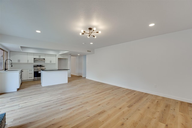 unfurnished living room with light wood-type flooring, an inviting chandelier, and sink