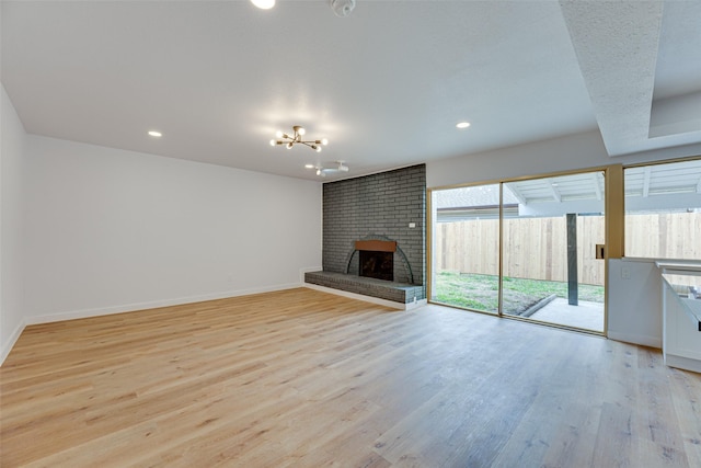 unfurnished living room featuring a brick fireplace, a notable chandelier, a wealth of natural light, and light hardwood / wood-style flooring