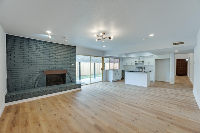 unfurnished living room featuring a textured ceiling, sink, light wood-type flooring, and a fireplace