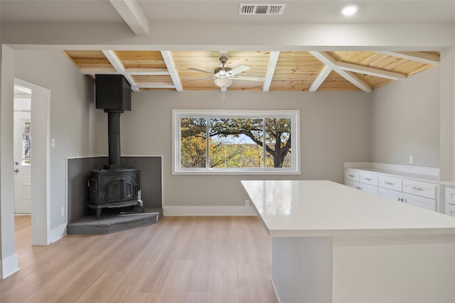 interior space featuring a wood stove, ceiling fan, wooden ceiling, lofted ceiling with beams, and light wood-type flooring