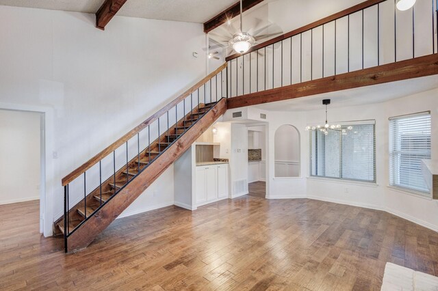 unfurnished living room featuring hardwood / wood-style flooring, ceiling fan with notable chandelier, beam ceiling, and high vaulted ceiling