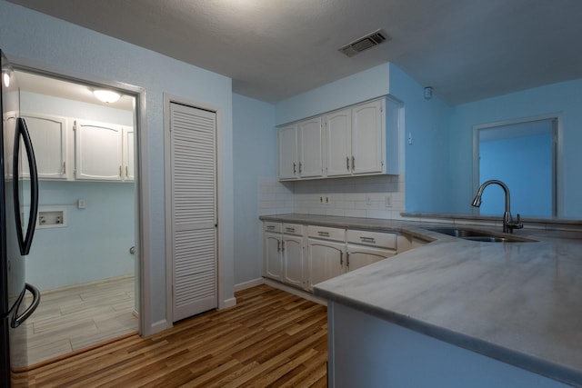 kitchen with white cabinets, sink, light hardwood / wood-style flooring, decorative backsplash, and stainless steel fridge