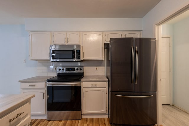 kitchen with white cabinets, decorative backsplash, stainless steel appliances, and light hardwood / wood-style flooring