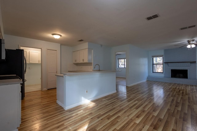 kitchen featuring black fridge, kitchen peninsula, a fireplace, white cabinets, and light wood-type flooring