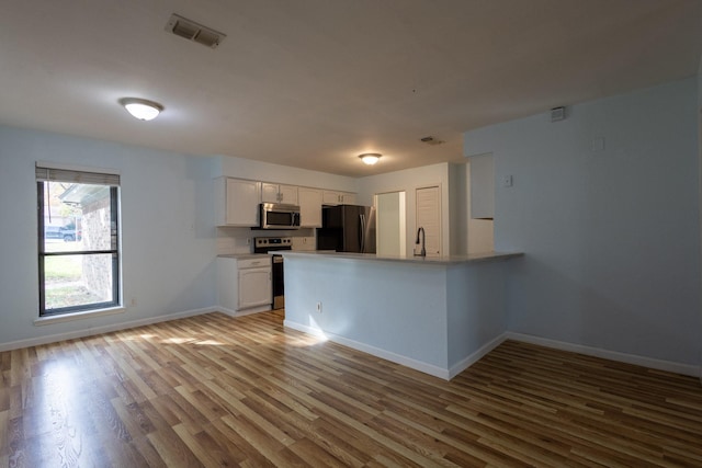 kitchen featuring white cabinetry, sink, stainless steel appliances, kitchen peninsula, and light wood-type flooring