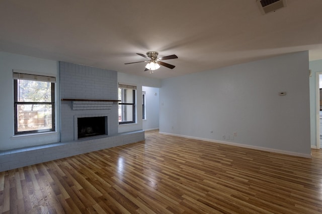 unfurnished living room featuring a wealth of natural light, dark hardwood / wood-style flooring, ceiling fan, and a brick fireplace