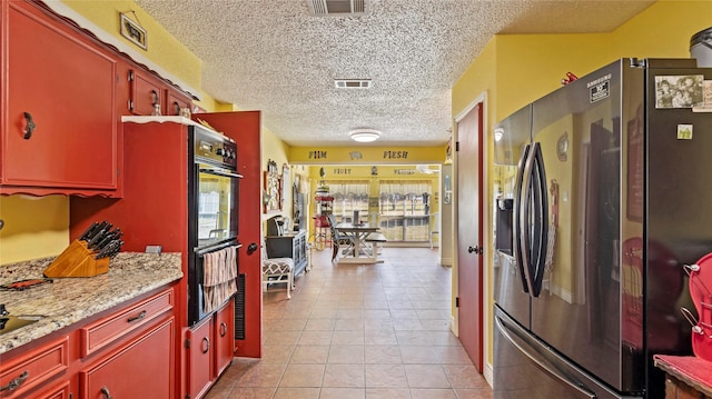 kitchen with light stone counters, a textured ceiling, double oven, light tile patterned floors, and stainless steel fridge with ice dispenser