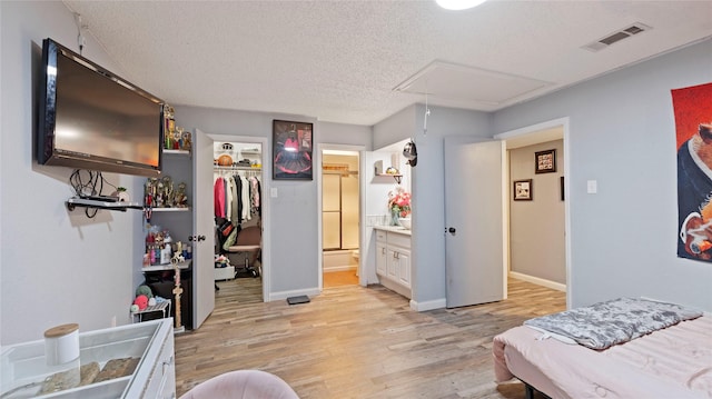 bedroom with light hardwood / wood-style floors, a textured ceiling, connected bathroom, and a closet