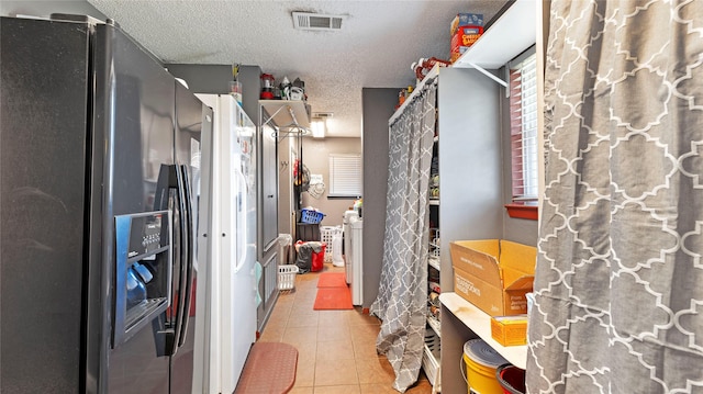 kitchen with a textured ceiling, light tile patterned floors, a healthy amount of sunlight, and stainless steel refrigerator with ice dispenser