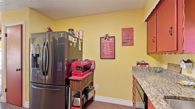 kitchen with a textured ceiling, stainless steel appliances, light stone counters, and light tile patterned flooring