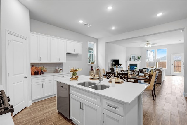 kitchen with dishwasher, a kitchen island with sink, sink, and white cabinets