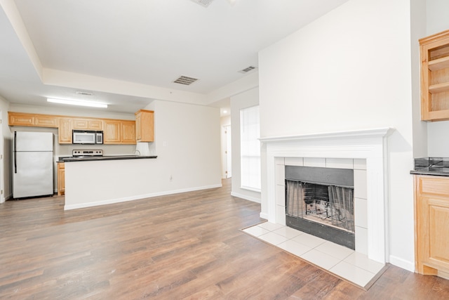 unfurnished living room featuring a tiled fireplace and light wood-type flooring