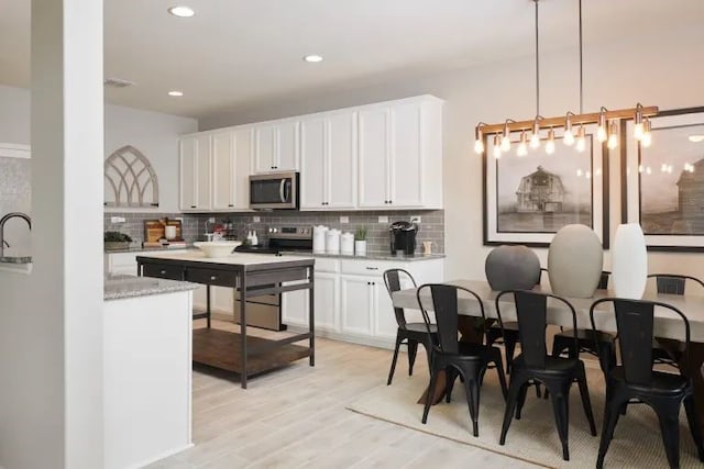 kitchen featuring pendant lighting, white cabinets, stainless steel appliances, and light hardwood / wood-style flooring