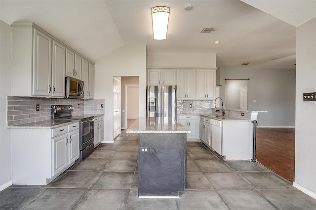 kitchen featuring sink, stainless steel appliances, vaulted ceiling, decorative backsplash, and a kitchen island