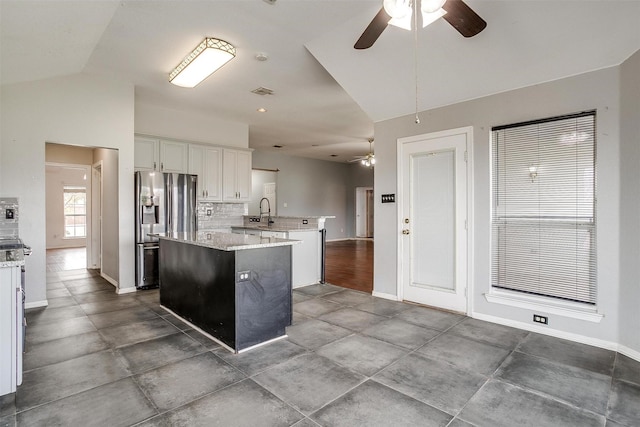 kitchen with light stone countertops, vaulted ceiling, stainless steel fridge with ice dispenser, white cabinetry, and an island with sink