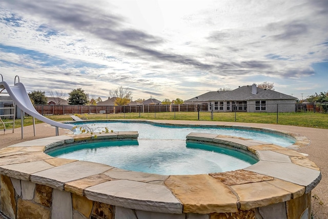 view of swimming pool with a yard, a hot tub, and a water slide