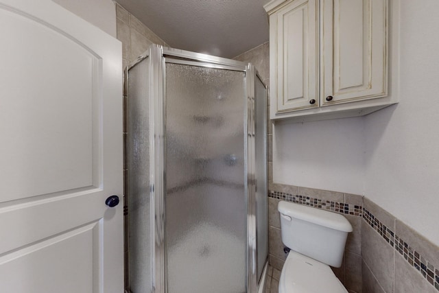 bathroom featuring tile walls, toilet, a shower with door, and a textured ceiling