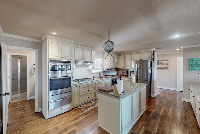 kitchen with pendant lighting, a center island, appliances with stainless steel finishes, ornamental molding, and light stone counters