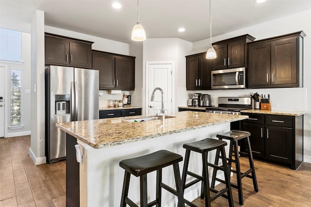 kitchen with light wood-type flooring, stainless steel appliances, a center island with sink, and sink