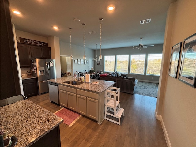 kitchen featuring a center island with sink, sink, light stone countertops, appliances with stainless steel finishes, and dark brown cabinets