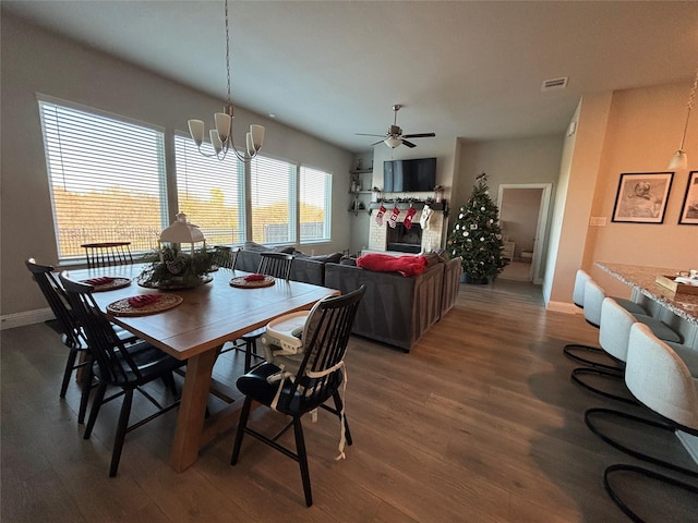 dining area featuring a fireplace, ceiling fan with notable chandelier, and dark hardwood / wood-style floors