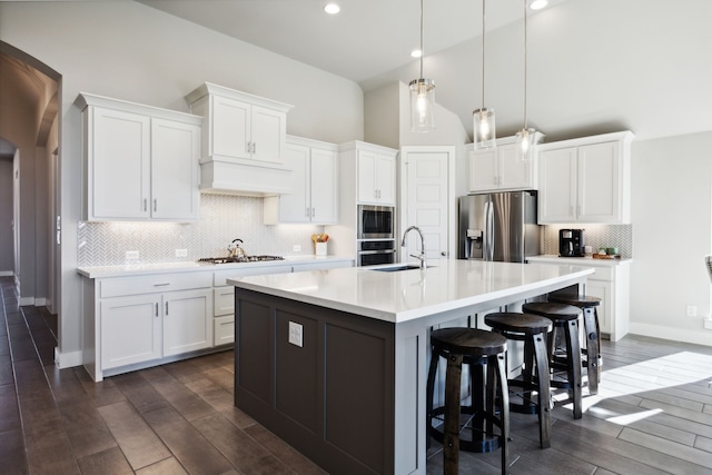 kitchen with white cabinets, appliances with stainless steel finishes, dark hardwood / wood-style floors, and an island with sink