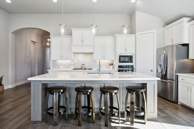 kitchen with hanging light fixtures, appliances with stainless steel finishes, a kitchen island with sink, and wood-type flooring