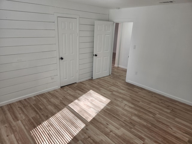 unfurnished bedroom featuring wooden walls, a closet, and light wood-type flooring